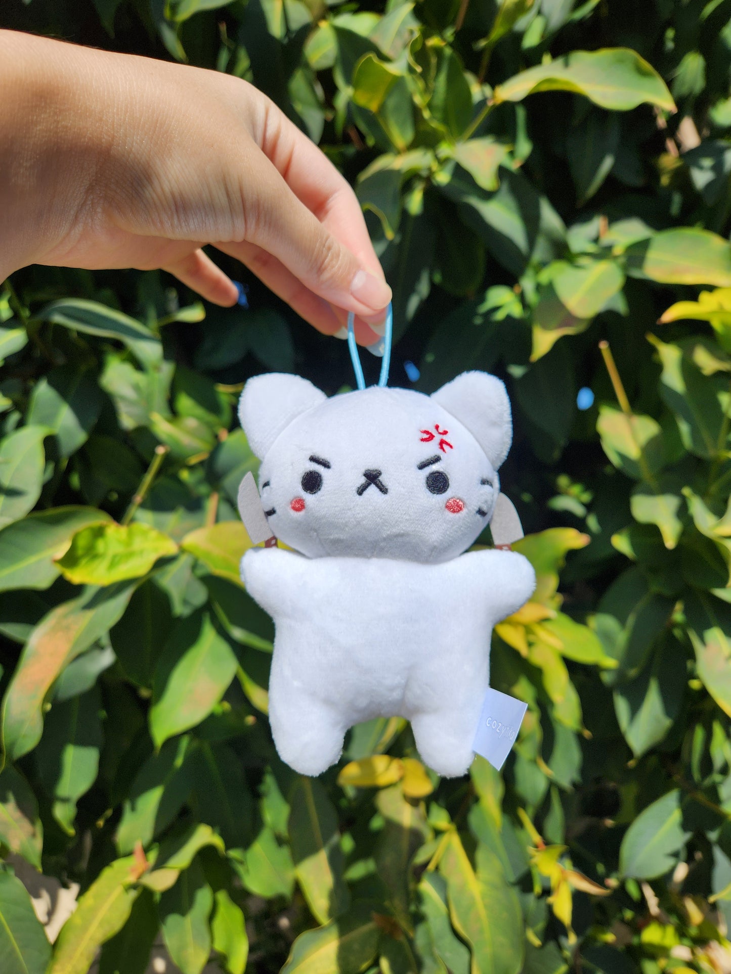 hand holding the elastic band of an angry white cat plushy with two knives